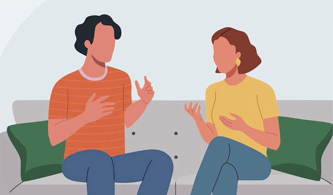 Two adults sat on a sofa talking to one another